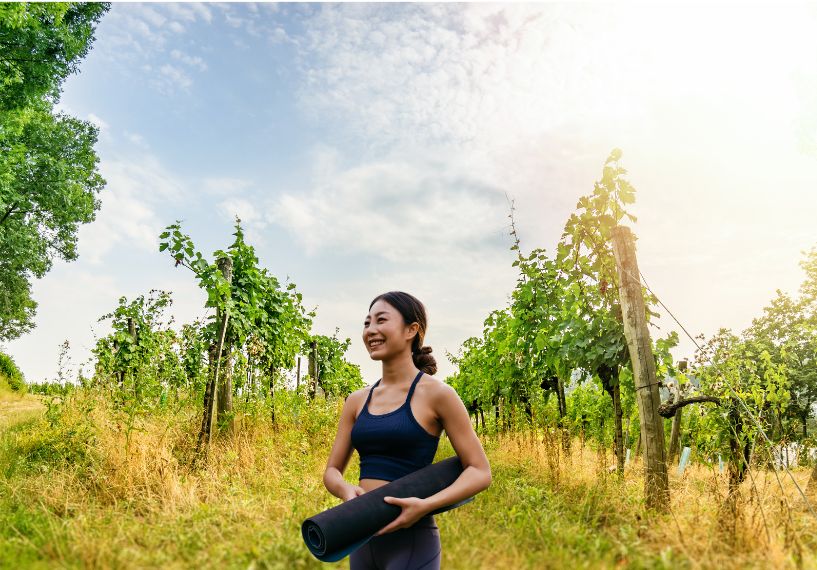 Yoga practitioner in a vineyard, holding her rolled up mat